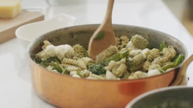 Yüzü olmayan kadın aşçıdan spatulayla makarna karıştırarak evdeki mutfaktaki masada spatula