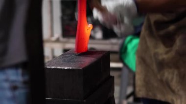 Eldivenli anonim bir zanaatkarın demirci atölyesinde çekici ile sıcak metal detayı yaparken çekilmiş görüntüler.