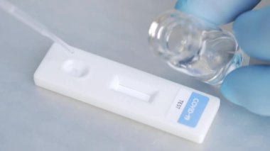 Yukarıda tanımlanamayan lateks eldivenli doktor ekspres koronavirüs test çubuğuna kimyasal reaktör düşürüyor ve testler negatif sonuç veriyor.
