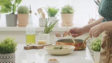 Kimliği belirsiz kadın aşçının iştah açıcı sıcak makarnayı evdeki mutfak masasında servis edişinin yan görüntüsü.