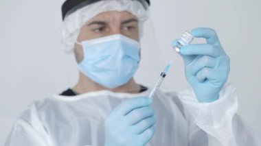 Ekin, modern donanımlı hastanede çalışırken cerrah önlüğü eldivenleri ve yüz kalkanı ile şırıngayı şişeden aldığı ilaçlarla dolduran profesyonel erkek tıp doktoru.