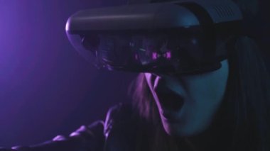 Uzamış kollu, VR kulaklık takan tanınmayan bir kadın, projektör aydınlatmasıyla duvarın yanındaki mavi neon ışığı altında sanal gerçekliği keşfediyor.