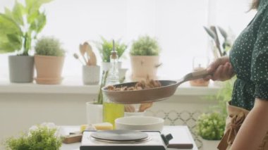 Gündüz vakti mutfakta öğle yemeği hazırlarken tavada ceviz pişirip kızartıp çırpan tanınmamış bir aşçının yan görüntüsü.