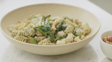 Anonim bir aşçı sofrada servis edilen pesto soslu ve yeşil fasulyeli iştah açıcı makarnaya ceviz serpiyor.