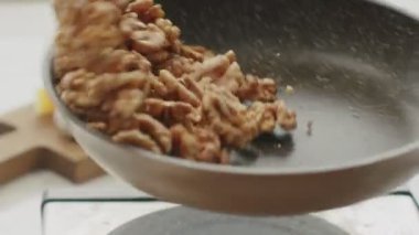 Gündüz vakti mutfakta öğle yemeği hazırlarken tavada ceviz pişirip kızartıp çırpan tanınmamış bir aşçıdan.