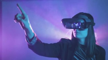 Uzamış kollu, VR kulaklık takan, projektör ışıklandırmasıyla duvarın yanındaki mavi neon ışığı altında sanal gerçekliği keşfeden tanınmamış bir kadının yan görüntüsü.