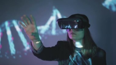 Uzamış kollu, VR kulaklık takan, projektör ışıklandırmasıyla duvarın yanındaki mavi neon ışığı altında sanal gerçekliği keşfeden tanınmamış bir kadının yan görüntüsü.