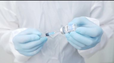 Ekin, modern donanımlı hastanede çalışırken cerrah önlüğü eldivenleri ve yüz kalkanı ile şırıngayı şişeden aldığı ilaçlarla dolduran profesyonel erkek tıp doktoru.