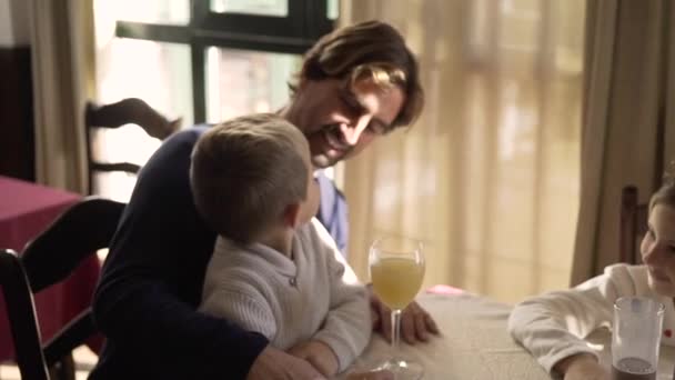 テーブルの上の幸せな小さな子供たちは 自宅で陽気な両親と朝食中に楽しく飲んでいます — ストック動画