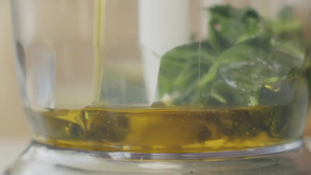キッチンでのペストソース調製中に新鮮な生のバジルの葉とブレンダーの透明なボウルにオリーブオイルを注ぐ認識できない人 — ストック動画