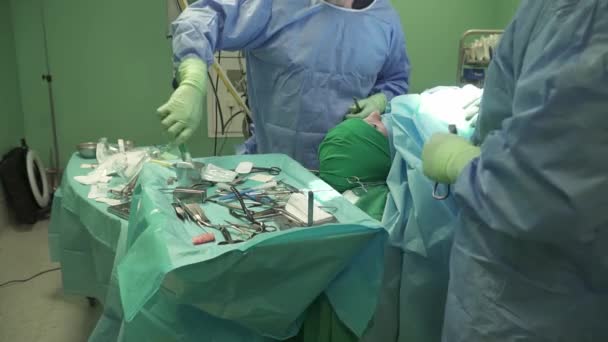 病院で手術を行う際に滅菌フィールドに散在する様々な楽器を選択するガウンとラテックス手袋の作物匿名外科医の上から — ストック動画