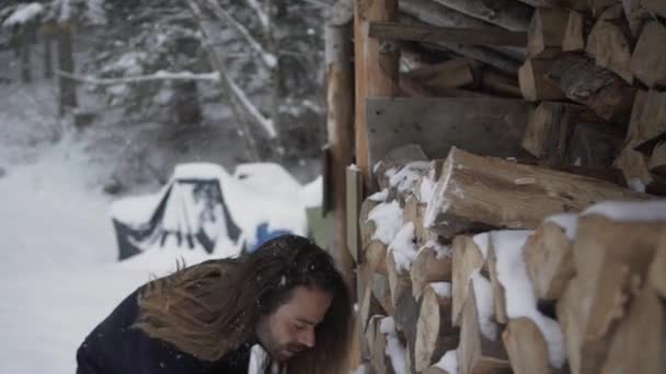 寒い冬の日に雪の中で薪を積んだ暖かい服を着た若者 — ストック動画