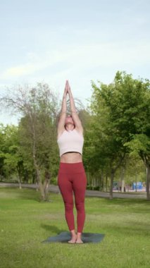Spor kıyafetleri içinde, yaz parkında yoga seansı sırasında paspasın üzerinde güneş seansı düzenleyen sağlıklı bir kadın resmi.