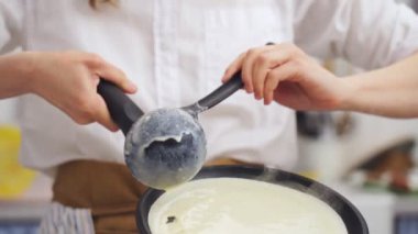 İsimsiz profesyonel aşçı mutfakta bir kepçeyle krep hamurunu tavaya koyuyor.