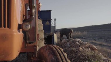 Yaşlı erkek çiftçi elinde büyük bir taşla ayakta duruyor.