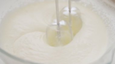 Beyaz bir masada, kasedeki hamuru döven iki vuruculu profesyonel bir mikserin yakın çekimi.