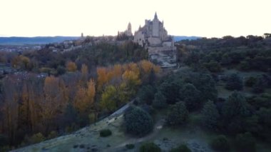 Sonbahar günbatımında İspanya 'nın Avila kentinde yol kenarındaki yemyeşil ağaçların arasında bulunan Segovia' lı yaşlı Alcazar 'ın insansız hava aracı görüntüsünden.