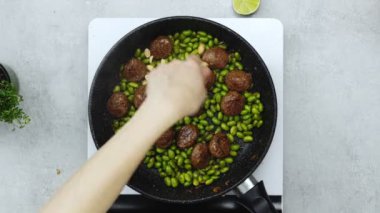 Meçhul kadın aşçının gerçek zamanlı görüntüsü portatif fırında tavada kızartılmış yeşil fasulyeli köftelere fıstık ekliyor.