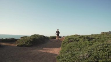 Gün batımında dağlarda spor kıyafetleri içinde koşan genç bir bayan koşucu. Deniz manzaralı. 