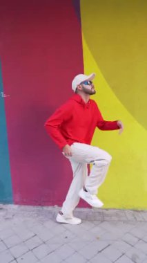 Kenar manzaralı, şık giysiler içinde sakallı erkek dansçı şehir caddesindeki duvarın yanındaki kaldırımda gösteri yapıyor.