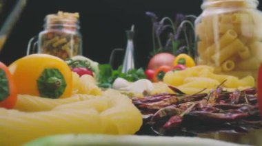 Closeup pan left shot of uncooked macaroni pasta arranged on table with fresh vegetables and leaves prepared for cooking