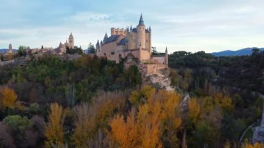 Sonbahar günbatımında İspanya 'nın Avila kentinde yol kenarındaki yemyeşil ağaçların arasında bulunan Segovia' lı yaşlı Alcazar 'ın insansız hava aracı görüntüsünden.