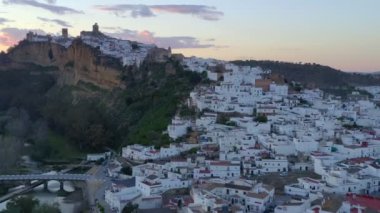 İspanya, Endülüs 'te bulutlu gün batımına karşı kayalıklarda bulunan Arcos de la Frontera kasabasının nefes kesici insansız hava aracı manzarası
