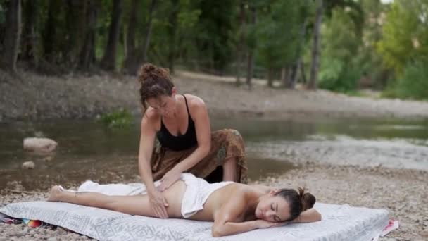 成年女按摩师穿着黑色上衣做臀部按摩 闭眼躺在池塘边的垫子上 — 图库视频影像