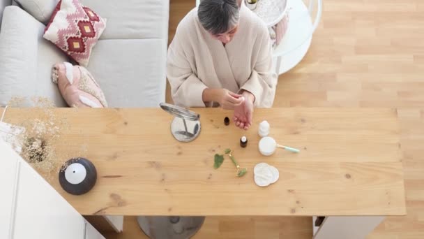 以上中年妇女在家中日常护肤时 穿着浴衣坐在餐桌旁 身上滴着血清的情景 — 图库视频影像