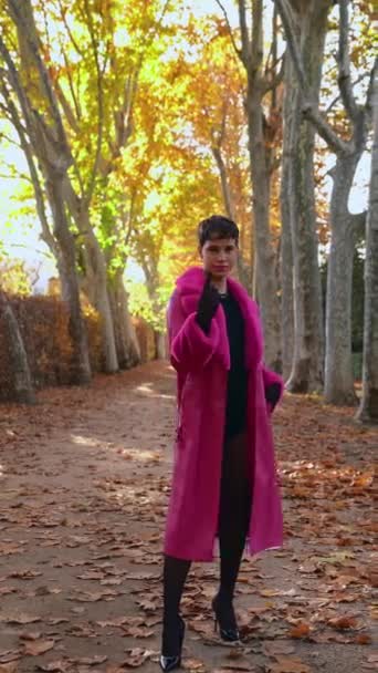 秋天公园里穿着鲜亮洋红色外套的非二元时尚人士手握食指招式手势 在布满干叶的小径上走来走去的跟踪镜头 — 图库视频影像