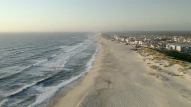 Portekiz 'in Mira kentindeki tatil köyünde kumlu plaja vuran köpüklü deniz dalgalarının nefes kesici drone görüntüsü.