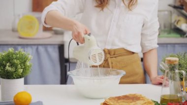 İsimsiz bir kadın şef, profesyonel bir mikser kullanıyor. Beyaz bir masada, kasede hamur dövüyor.
