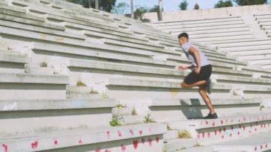 Güneşli bir parkta spor gününde spor kıyafetli, beton merdivenlerden koşarak çıkan güçlü etnik erkek görüntüsü.