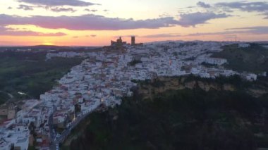 İspanya, Endülüs 'te bulutlu gün batımına karşı kayalıklarda bulunan Arcos de la Frontera kasabasının nefes kesici insansız hava aracı manzarası