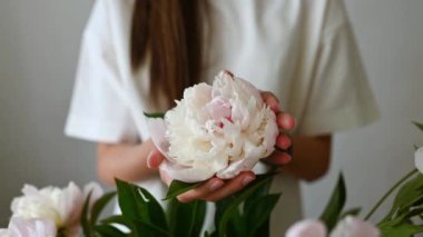 Kırpılmış isimsiz bir kız elinde çiçek açan yeşil yapraklı bir çiçekle elinde ahşap bir masa ile duruyor.