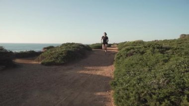 Gün batımında dağlarda spor kıyafetleri içinde koşan genç bir bayan koşucu. Deniz manzaralı. 