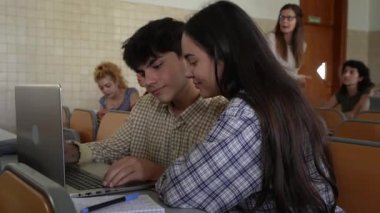 Genç sınıf arkadaşları masada oturuyor ve üniversitedeki bir sınıfta dizüstü bilgisayar kullanarak proje üzerinde çalışıyorlar.