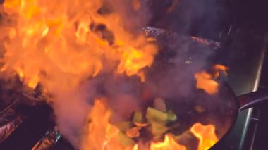 Mutfakta yanan ateşin üzerinde lezzetli yemekler hazırlarken, sebzeleri kızartma tavasında karıştıran isimsiz şefin yavaş çekimleri.