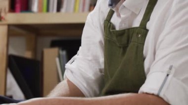 Genç erkek terzi, çağdaş atölyenin bulanık iç mekânına karşı masada özel giyim koleksiyonu üzerinde çalışırken gelecekteki kıyafetlerin detaylarını geliştiriyor.