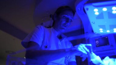 Ekin taşıyan, elinde küçük bir bebek taşıyan ve şişeyle beslenen bir kadının yan görüntüsü. Bağımlılık yapan hastanedeki tıbbi ekipmanlara karşı küçük hastane yataklarının yanında dururken.