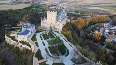 İspanya 'nın Avila kentinde sonbaharda yolun kenarındaki tepedeki yemyeşil ağaçların arasında bulunan yaşlı Segovia Alcazar' ın insansız hava aracı görüntüsü.