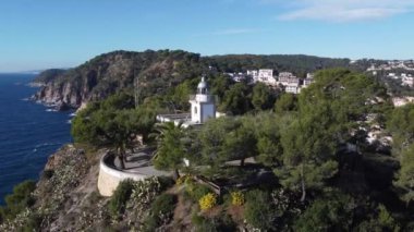 Girona 'da güneşli bir günde muhteşem mavi denize bakan kayalık kayalıklara bakan kulesi olan beyaz kilisenin resimli hava manzarası.