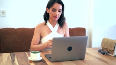 Kadın girişimci cep telefonuyla iş projesini tartışırken netbook kullanıyor ve kafedeki masada uzaktan çalışıyor.