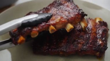 Mutfaktaki tabağa tavadan pirzola koymak için maşa kullanan tanınmamış bir insanın üst görüntüsü.