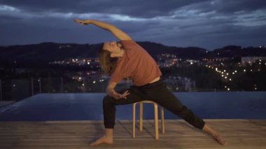 Aktif kıyafetli sakin bir adam, akşam vakti havuzun yanındaki terasta birlikte yoga yaparken yoga yapıyor.