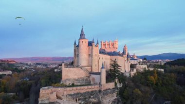 İspanya 'nın Avila kentindeki bulutlu günbatımına karşı Segovia Alcazar yakınlarında uçan paraglider hava görüntüsünü yükselt