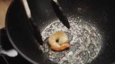 Mutfakta lezzetli bir akşam yemeği hazırlarken tavadan tavaya taze kızarmış karides atarak isimsiz bir aşçının üstünden.