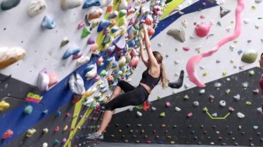 Spor giyim sektöründe kadın dağcıdan parlak tutacaklarla kaya duvarına tırmanırken, spor salonundaki antrenman sırasında arkadaşı yerde rehberlik ediyordu.