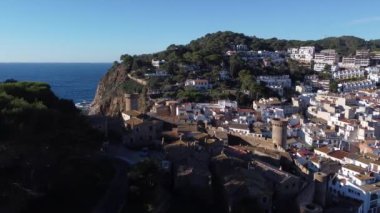 İspanya 'nın güneşli bir gününde, kıyı kasabasında kumlu sahili yıkayan köpüklü dalgalarla denizin üzerindeki kayalık kayalıkların muhteşem hava manzarası.