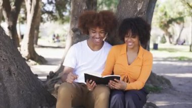 Mutlu Afro-Amerikan erkek ve kadın gündelik giysiler içinde oturmuş Ciutadella Park 'ta vakit geçirirken ağaç gövdesinde kitap izliyorlar.